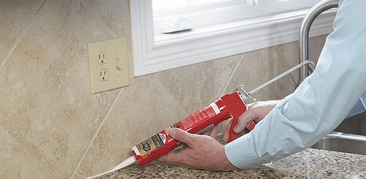 Handyman applying caulk along a kitchen backsplash and countertop seam in Ogden, UT