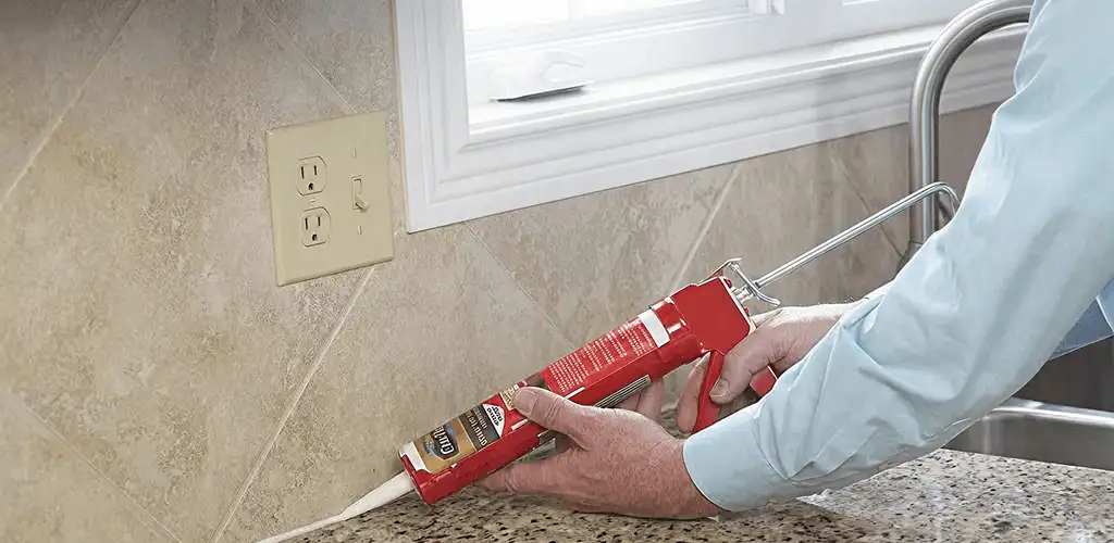 Handyman applying caulk along a kitchen backsplash and countertop seam in Ogden, UT