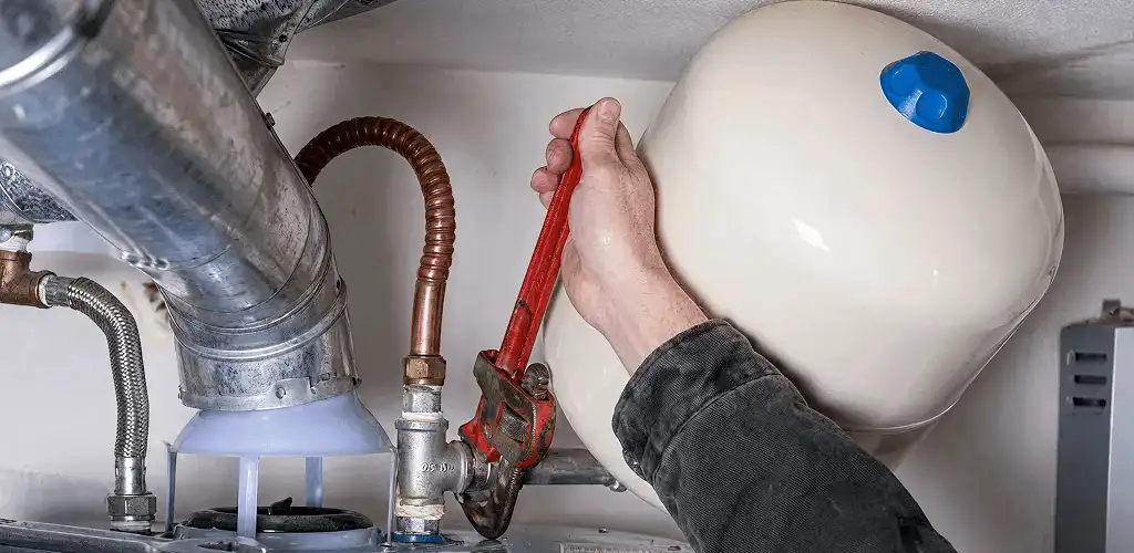 Water heater repair technician tightening plumbing connections near a tank unit in Ogden, UT